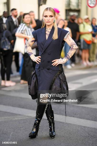 Guest wears diamonds and emeralds pendant earrings, a black striped print pattern sleeveless / buttoned jacket dress with embroidered black puffy...