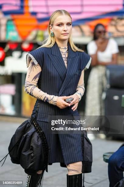 Camille Razat wears diamonds and emeralds pendant earrings, a black striped print pattern sleeveless / buttoned jacket dress with embroidered black...