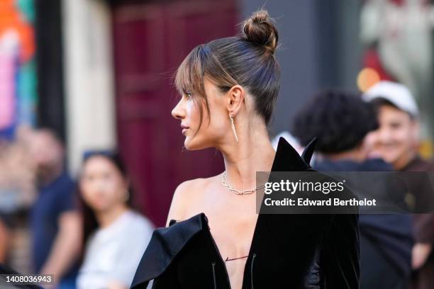 Alessandra Ambrosio wears gold and diamonds pendant earrings, a black velvet asymmetric V-neck / one shoulder-off / long sleeves velvet dress, a gold...