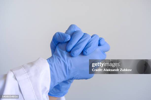 the hands of the attending physician or paramedic in medical rubber gloves against a white wall, close-up. a doctor in a medical uniform with clenched hands. the concept of healthcare, pharmacy, healthcare and medicine. copy space. - surgical glove stock pictures, royalty-free photos & images