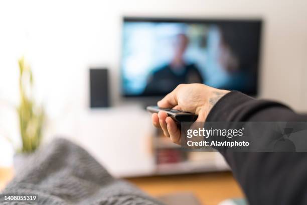man on sofa changing tv channel - fernsehen stock-fotos und bilder