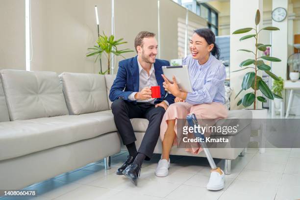 an asian female white collar worker with prosthetic leg having conversation with her colleague during coffee break. - disabled accessibility stock pictures, royalty-free photos & images
