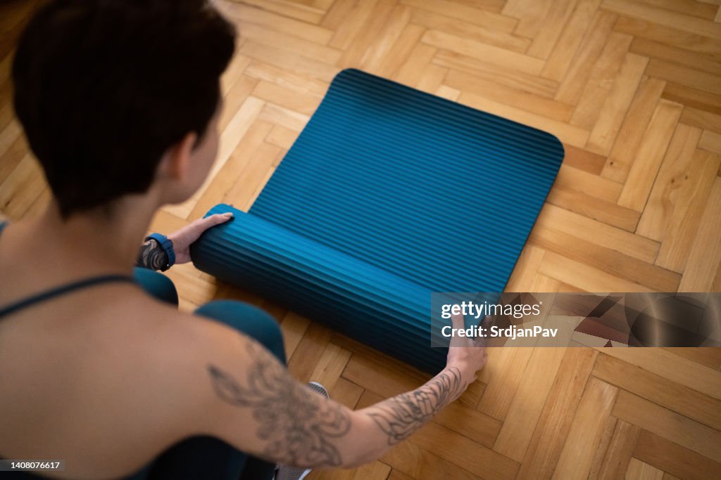 Young Caucasian female sportsperson, preparing her yoga mat, for home workout