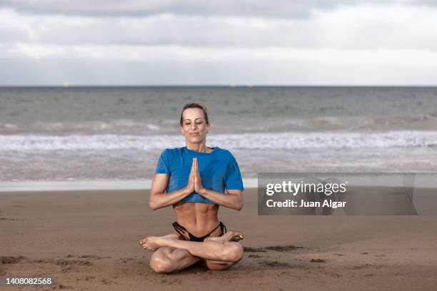 calm fit lady meditating in lotus pose with closed eyes on sandy beach - namaste stock pictures, royalty-free photos & images