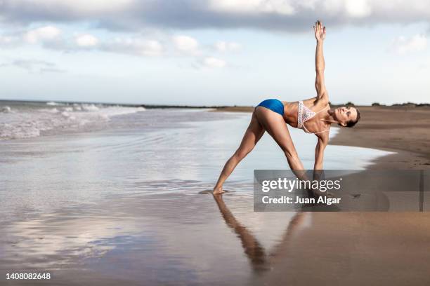 slim lady performing revolved triangle asana during yoga session on seashore - parivrtta trikonasana stock pictures, royalty-free photos & images