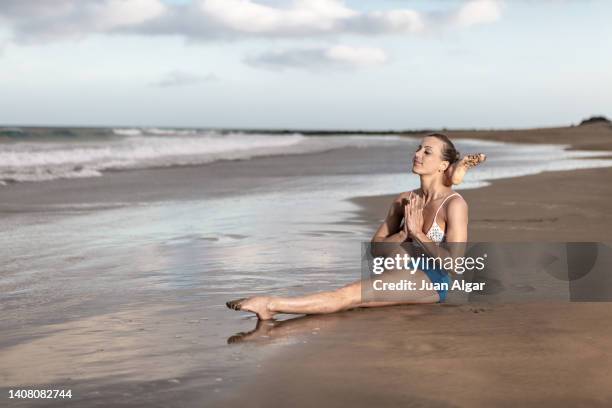 calm fit lady meditating in eka pada shirshasana a yoga pose on seashore - shirshasana stock pictures, royalty-free photos & images