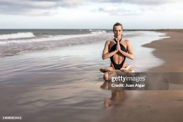 flexible lady performing padmasana pose with prayer hands near wavy sea - inviting gesture stock pictures, royalty-free photos & images