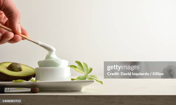 hand with stick taking avocado moisturizing cream on white plate - esteticista fotografías e imágenes de stock