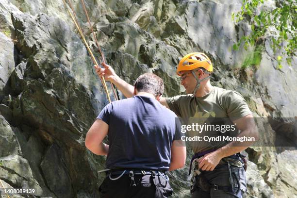 man mentoring boy and teaching him to tie knots for rock climbing - zekeren stockfoto's en -beelden