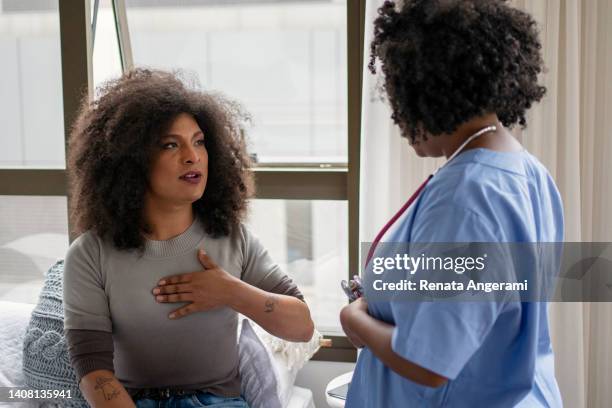 nurse examining transgender woman at home - homocultuur stockfoto's en -beelden