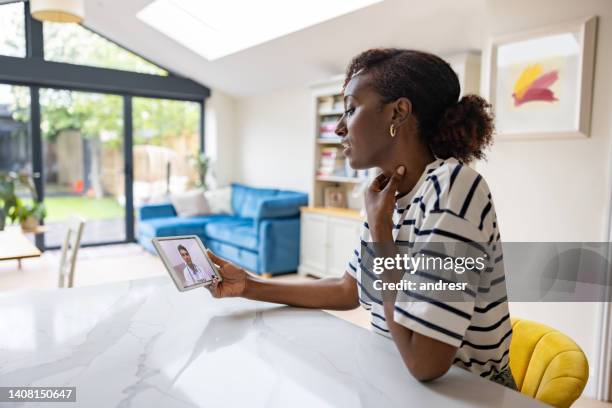 woman at home talking a dictor about her sore throat on a video call - ehealth stockfoto's en -beelden