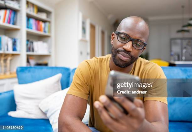 homme se relaxant à la maison en regardant les médias sociaux sur son téléphone portable - completely bald stock photos et images de collection