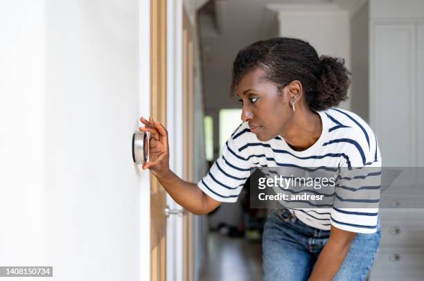 mujer ajustando la temperatura en el termostato de su casa - eficiencia energetica fotografías e imágenes de stock