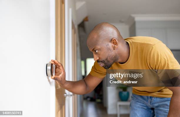 man adjusting the temperature on the thermostat of his house - eficiência energética imagens e fotografias de stock