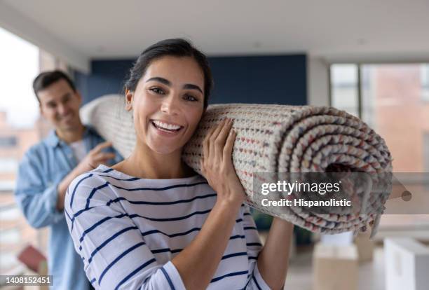 happy couple moving house and carrying a rolled up carpet - carpets stock pictures, royalty-free photos & images