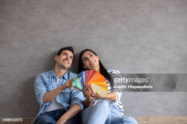 couple at home thinking about painting the walls and holding a color swatch - contemplation family stockfoto's en -beelden