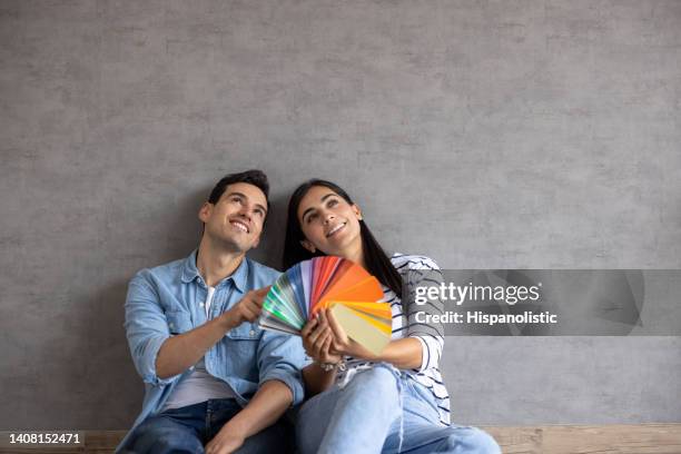 couple at home thinking about painting the walls and holding a color swatch - contemplation family imagens e fotografias de stock