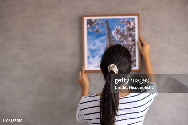 donna che decora la sua casa e appende un quadro incorniciato al muro - appendere quadro foto e immagini stock