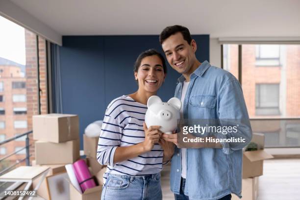 happy couple moving house and saving in a piggy bank - happy couple at home stockfoto's en -beelden