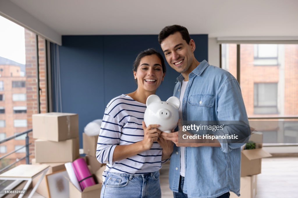 Happy couple moving house and saving in a piggy bank