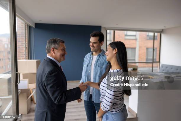 real estate agent selling an apartment to a couple and closing the deal with a handshake - real estate broker stock pictures, royalty-free photos & images