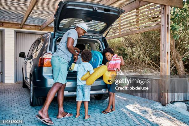 una familia empacando el coche para salir de vacaciones de verano. un feliz padre afroamericano y sus dos lindos hijos pequeños preparando el equipaje en su vehículo para ir en un viaje por carretera, listos para el tiempo de viaje. - viaje por carretera fotografías e imágenes de stock