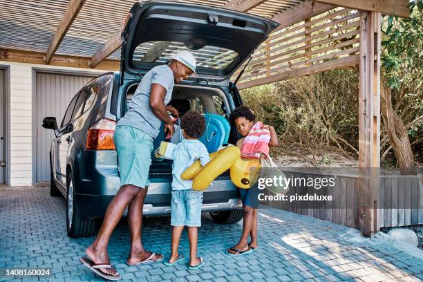 une famille emballant la voiture pour partir en vacances d’été. un père afro-américain heureux et ses deux mignons petits fils préparant les bagages dans son véhicule pour partir en road trip, prêts pour le temps de voyage - vacances photos et images de collection