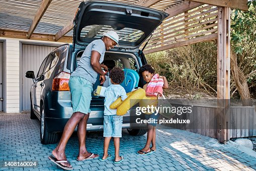 A family packing the car to leave for summer vacation. A happy african american father and his two cute little sons preparing the luggage in his vehicle to go on a road trip, ready for travel time A family packing the car to leave for summer vacation. A happy african american father and his two cute little sons preparing the luggage in his vehicle to go on a road trip, ready for travel time