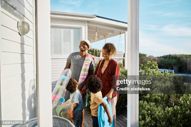 a happy family arriving at a holiday home for their summer vacation. husband and wife smiling and holding toys and towels taking their two cute sons to the beach on a sunny day during holidays - happy holidays family stock pictures, royalty-free photos & images
