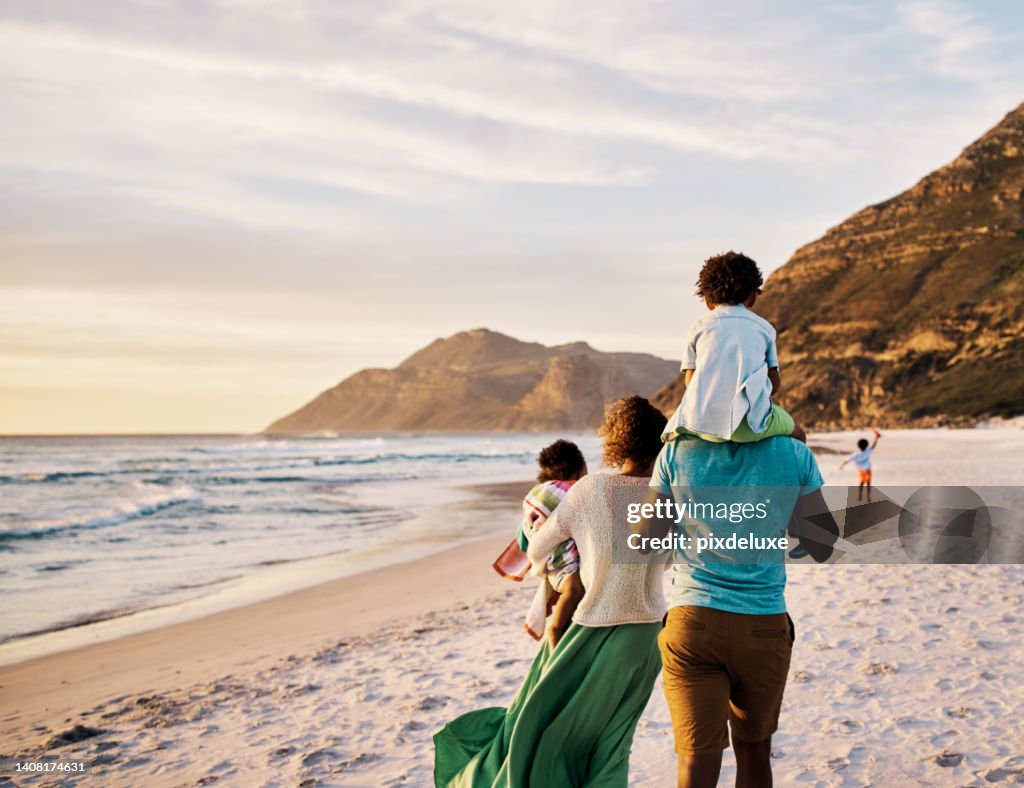 African parents with little kids bonding and strolling by ocean. Little children enjoying the outdoors during their summer holidays or vacation. Rear of a family walking on the beach with copy space