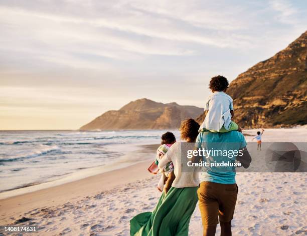 african parents with little kids bonding and strolling by ocean. little children enjoying the outdoors during their summer holidays or vacation. rear of a family walking on the beach with copy space - travel family imagens e fotografias de stock