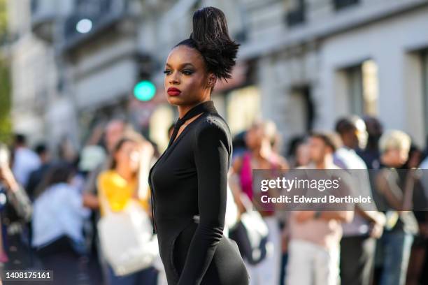 Guest wears diamonds earrings, a black tie, a black V-neck / long sleeves / shoulder-pads / long mermaid dress, outside Jean-Paul Gaultier, during...