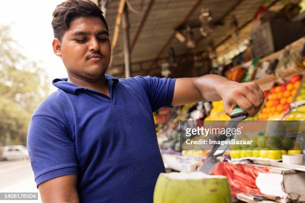 young man peeling coconut fruit at market - fruta tropical - fotografias e filmes do acervo