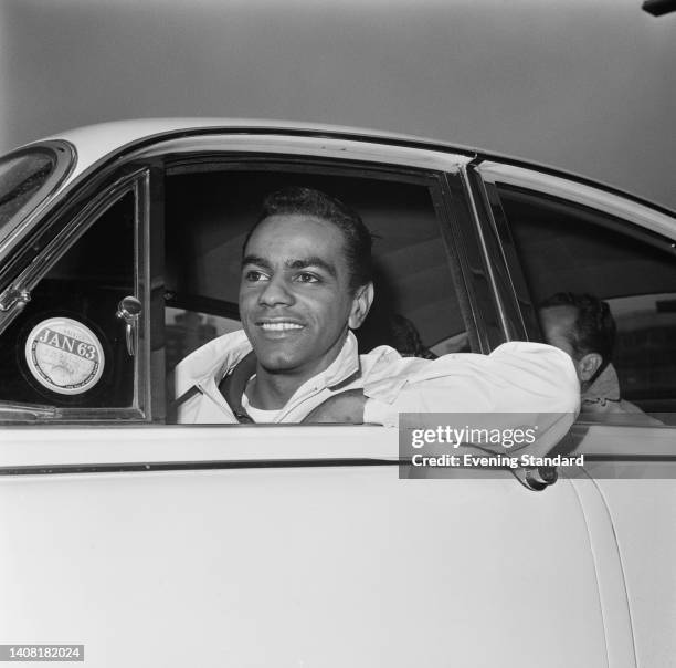 American singer Johnny Mathis, wearing a white jacket, his left elbow resting on the door of the car in which he is travelling as he arrives at...