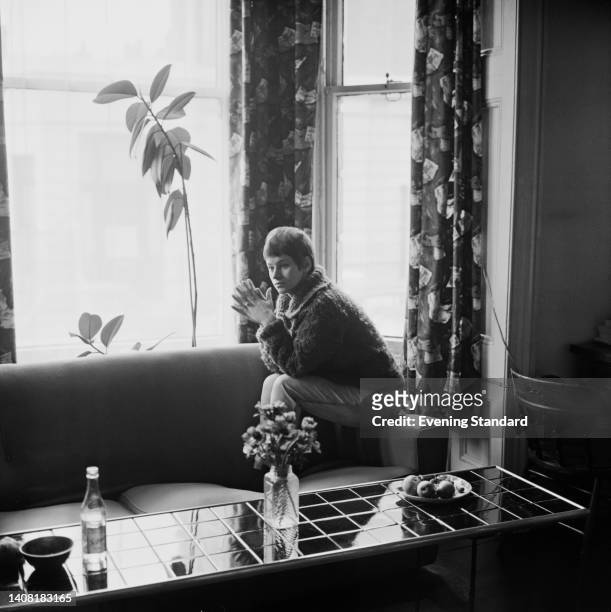 British actress Rita Tushingham, wearing a chunky knit sweater, as she sits on the armrest of a sofa in the living room of her home, United Kingdom,...