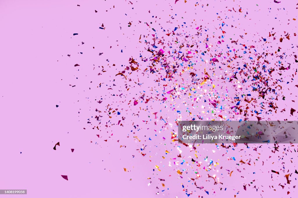 Colorful glitter confetti on a pink background.