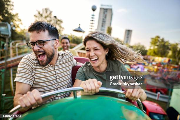 joven pareja alegre divirtiéndose en una montaña rusa en el parque de atracciones. - montaña rusa fotografías e imágenes de stock