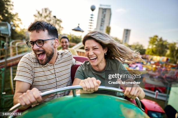 young cheerful couple having fun on rollercoaster at amusement park. - attractiepark stockfoto's en -beelden