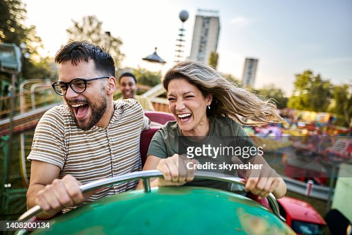 Young cheerful couple having fun on rollercoaster at amusement park.
