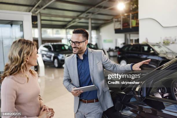 happy salesman selling the car to his female customer in a showroom. - car dealership stock pictures, royalty-free photos & images