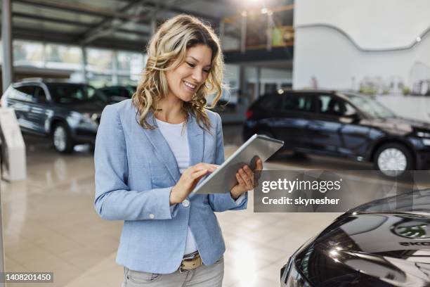 happy car salesperson using digital tablet in a showroom. - saleswoman stock pictures, royalty-free photos & images
