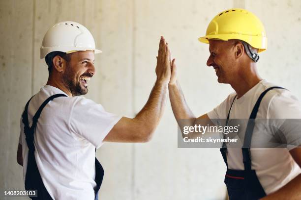 cheerful manual workers giving each other high-five at construction site. - construction-worker stockfoto's en -beelden
