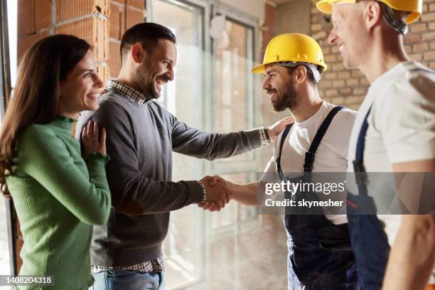los trabajadores manuales felices llegaron a un acuerdo con una pareja en el sitio de construcción. - building contractor fotografías e imágenes de stock
