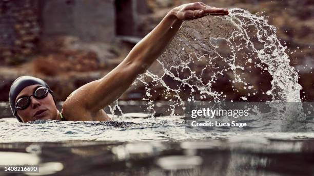 water splashes caught in motion with a female swimmer enjoying a sunset sea swim - swimming goggles stock pictures, royalty-free photos & images