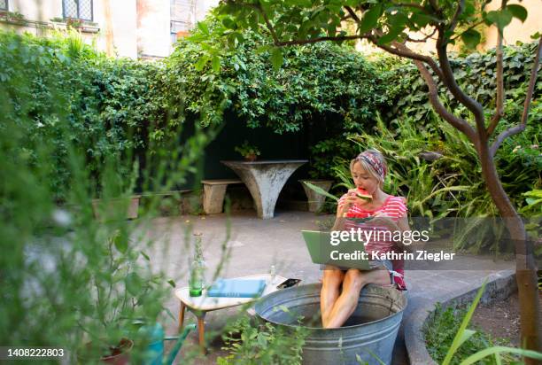 woman cooling off during heat wave with her feet in cold water, using laptop - mature woman in water stock pictures, royalty-free photos & images