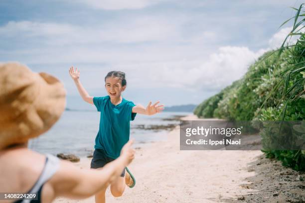 young girl running towards her mother on beach - île de taketomi photos et images de collection