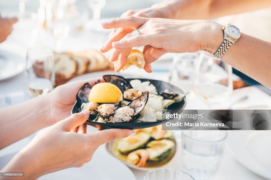 Close up of a woman's hand squeezing lemon juice on to mussels, enjoying meal in a restaurant.