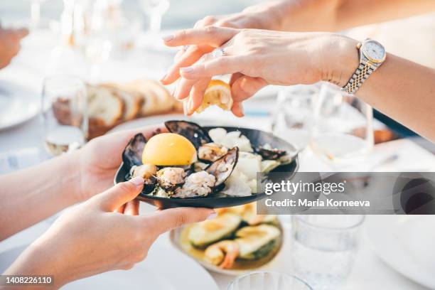 close up of a woman's hand squeezing lemon juice on to mussels, enjoying meal in a restaurant. - mediterranean food stockfoto's en -beelden