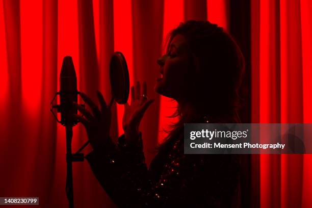 silhouette female singer singing and recording songs in recording studio in red glowing background - musique soul photos et images de collection