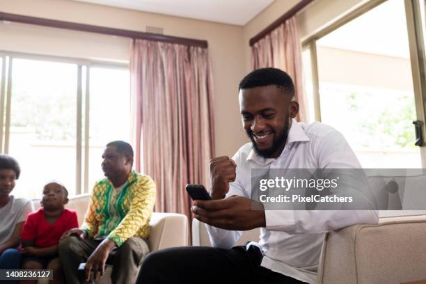 father celebrating his winnings on an app with rest of family - fist pumping stockfoto's en -beelden